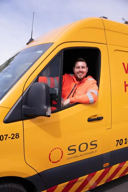 Autoredder sidder i teknikerbil og smiler